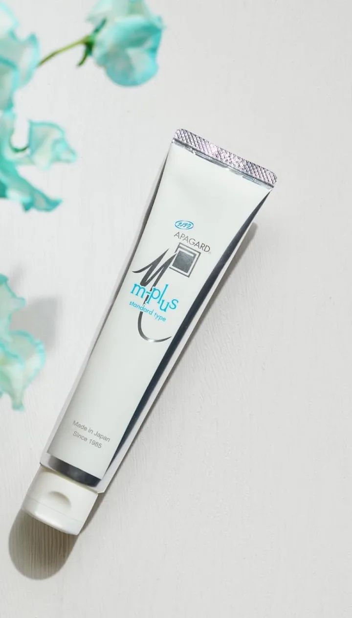 Apagard M-plus tube lying on a pale table beside blue flowers