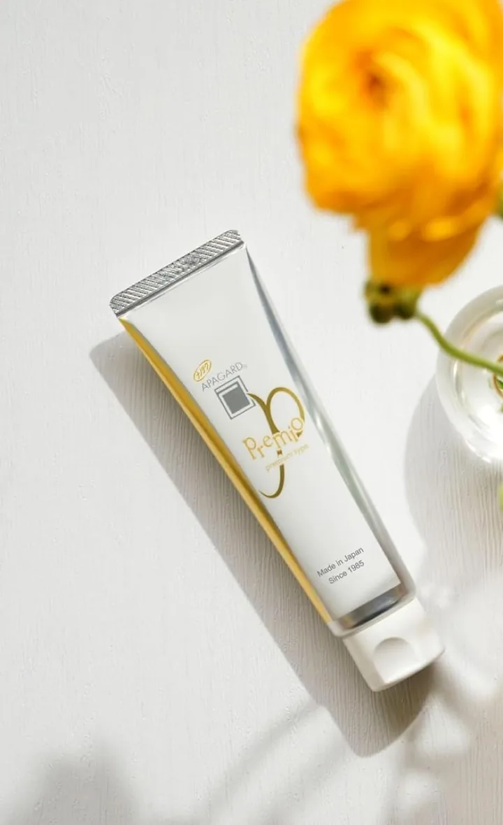 Apagard Premio tube lying on a pale table under a yellow flower